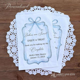 Boy baby shower favor bags adorned with a blue bow and frame printed on white paper bags.  Each is personalized with 'Babies are Sweet enjoy a treat, thank you for making my day complete'.  Mother to be's name and event date also printed.