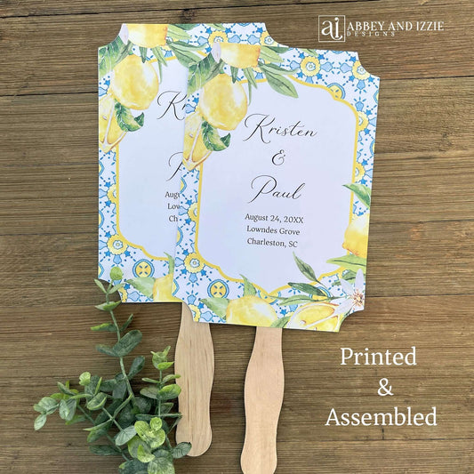 Our Amalfi Coast wedding fans personalized are printed on white stock adorned with lemons and blue tiles to match your Mediterranean Theme wedding. Fans are personalized for the bride and groom, two sided with handle hidden between. They come fully assembled and ready for your special day.