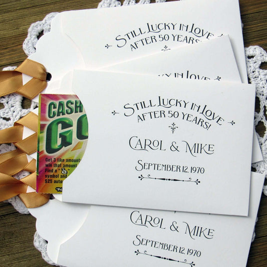 Our Lucky In Love 50th Anniversary Favors are personalized for the happy couple. Still lucky in lover after 50 years printed on white envelopes with gold ribbon attached. Slide a lottery ticket in the open end for a fun favor guest will love.