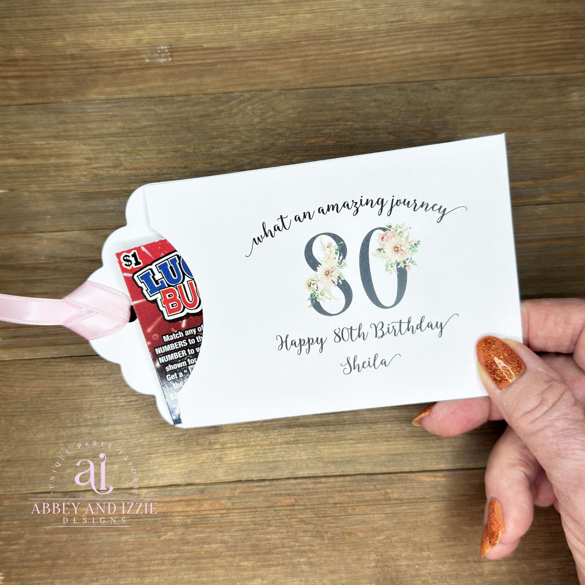 Milestone 80th Birthday Party Favors,  white envelopes adorned with 80 in a floral design, personalized for the guest of honor.  Slide a lottery ticket inside for a fun favor.  Your choice of ribbon color, white, pink or black.