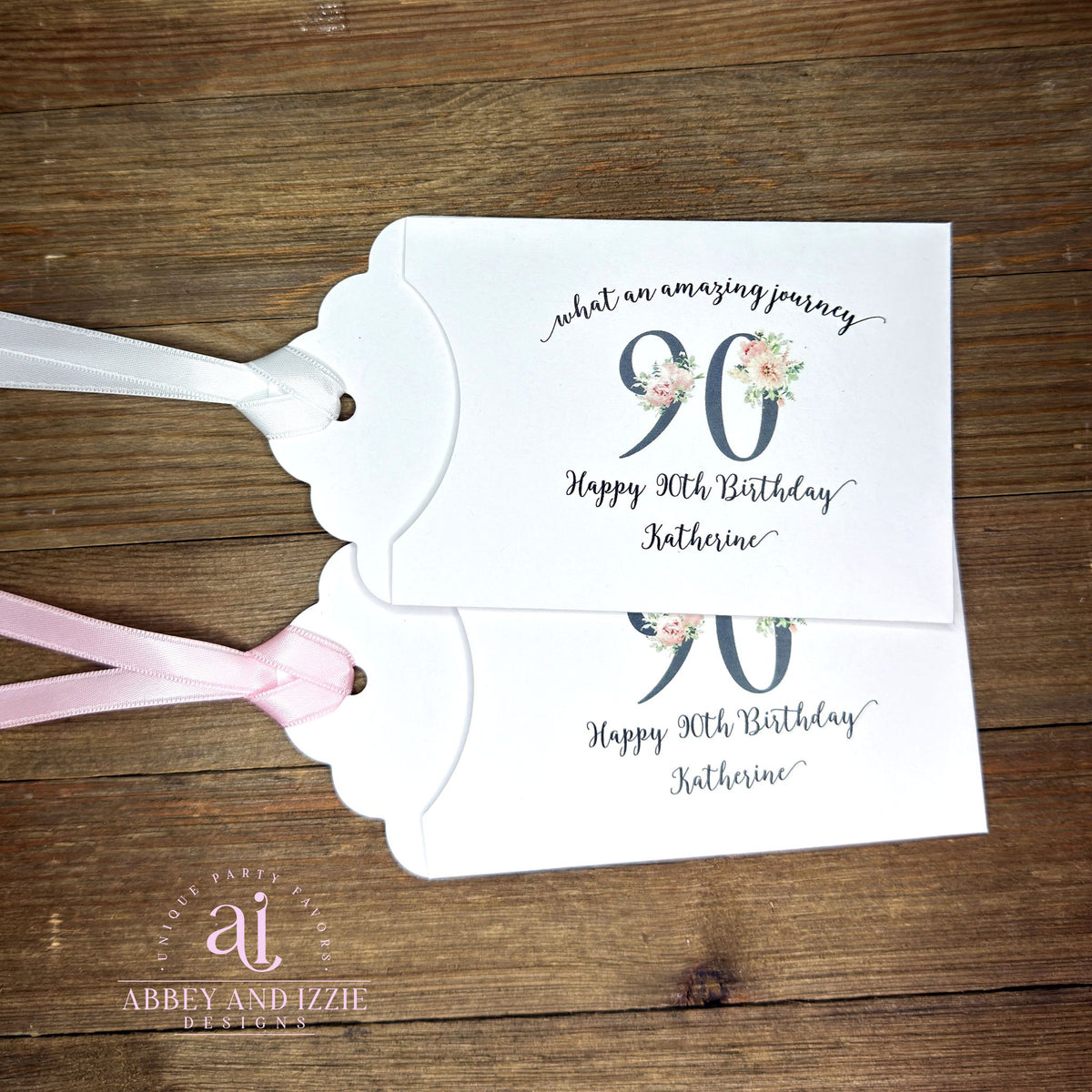 Elegant 90th Birthday Party Favors will add a special touch to your event.  Printed on white card stock with a large 90 in floral font add the guest of honors name for a personal touch.  Your choice of pink, black or white ribbon which comes attached