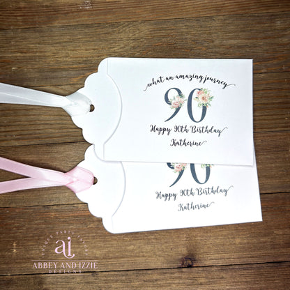 Elegant 90th Birthday Party Favors will add a special touch to your event.  Printed on white card stock with a large 90 in floral font add the guest of honors name for a personal touch.  Your choice of pink, black or white ribbon which comes attached