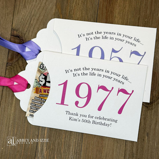 Personalized scratch-off birthday favors for adults. Each envelope features a special message with the year the guest of honor was born in color. Including a thank you for celebrating with the us. Works for milestone birthdays, adult parties, and special events see our store for more options. Constructed from white high-quality cardstock with your choice of year color and ribbon color, which comes attached.