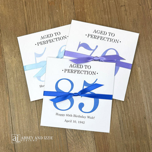These interactive Aged to Perfection scratch-off holders transform birthday celebrations into memorable moments. Guests scratch off the lottery ticket inside to reveal who the big winner is!&nbsp; Perfect for 50th, 60th, 70th birthdays, available for any birthday. Fully customizable with name, dates, and special messages tailored to the guest of honor. Printed on sturdy white cardstock ensures durability throughout your party. Your choice of large number color as well as the ribbon color to match your party