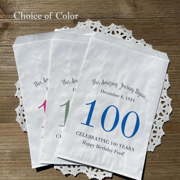 Personalized 100th birthday party favor bags, each with the name of the honoree and birth date printed.  Bags are white with a large 100 in color printed in the center.  Bags are larger than most and can hold hold cookies, candy, popcorn, goodies or even napkins and utensils.  