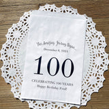 Personalized 100th birthday party favor bags, each with the name of the honoree and birth date printed.  Bags are white with a large 100 in color printed in the center.  Bags are larger than most and can hold hold cookies, candy, popcorn, goodies or even napkins and utensils. 