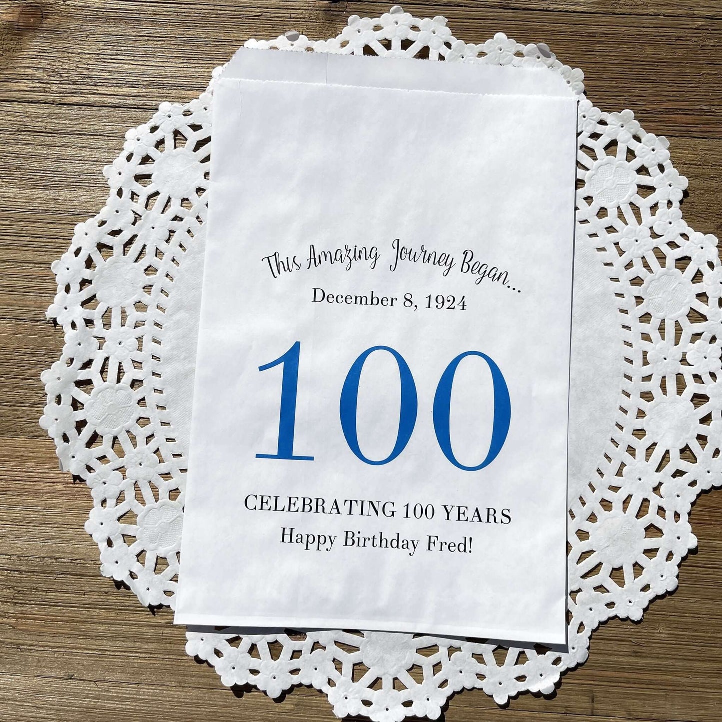  Personalized 100th Birthday Party Favor Bags, each with the name of the honoree and birth date printed.  Bags are white with a large 100 in color printed in the center.  Bags are larger than most and can hold hold cookies, candy, popcorn, goodies or even napkins and utensils.  