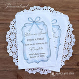 Boy baby shower favor bags adorned with a blue bow and frame printed on white paper bags.  Each is personalized with 'Babies are Sweet enjoy a treat, thank you for making my day complete'.  Mother to be's name and event date also printed.  