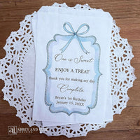 Personalized first birthday party favor bags, 'one is sweet, enjoy a treat, thank you for making my day complete'.  Printed on white paper bags and adorneed with a blue bow and border these will add a touch of elegance to the treat table. 