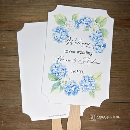Elevate your wedding ambiance with our personalized blue hydrangea fans, beautifully crafted to complement your special day.  Printed on white card stock with 'welcome to our wedding' and the bride and grooms names with wedding date printed. 