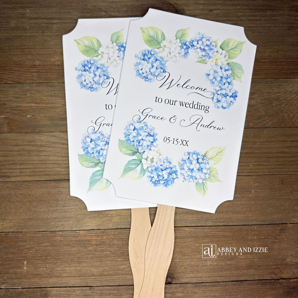 Elevate your wedding ambiance with our personalized blue hydrangea fans, beautifully crafted to complement your special day.  Printed on white card stock with 'welcome to our wedding' and the bride and grooms names with wedding date printed. 
