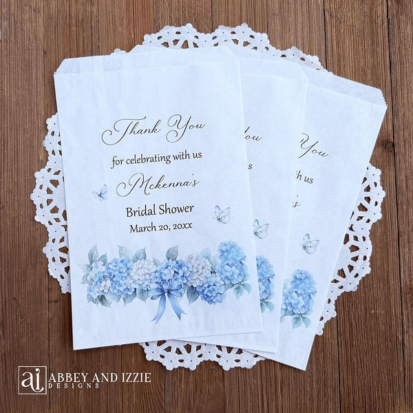 Personalized blue hydrangea bridal shower favors bags, perfect for a small gift of appreciation or a cookie bar or even a candy bar.  White bags adorned with delicate blue hydrangeas for a sweet addition to your event.