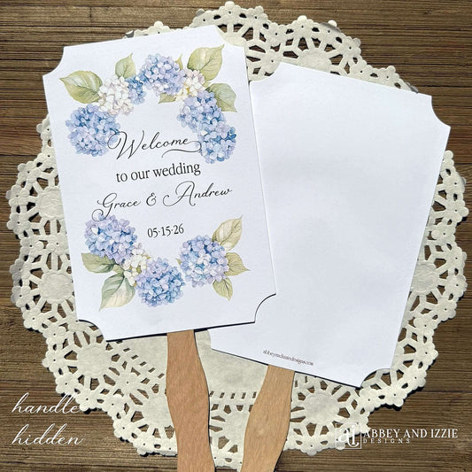 Elevate your wedding ambiance with our personalized blue hydrangea fans, beautifully crafted to complement your special day.  Printed on white card stock with 'welcome to our wedding' and the bride and grooms names with wedding date printed.  Fans ship assembled to you and are two sided, printing on one side only, handle hidden between the layers for a finished look. 