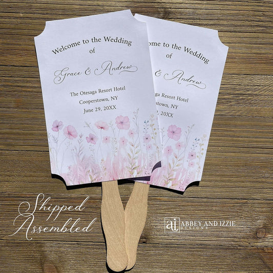 Blush pink wedding fans personalized, printed on white card stock with soft pink flower at the bottom.  Fans are personalized for the bride and groom and includes, place, city, state and date of your wedding.  They arrive fully assembled and ready for your day.