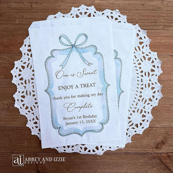 Personalized first birthday party favor bags, 'one is sweet, enjoy a treat, thank you for making my day complete'.  Printed on white paper bags and adorneed with a blue bow and border these will add a touch of elegance to the treat table. 