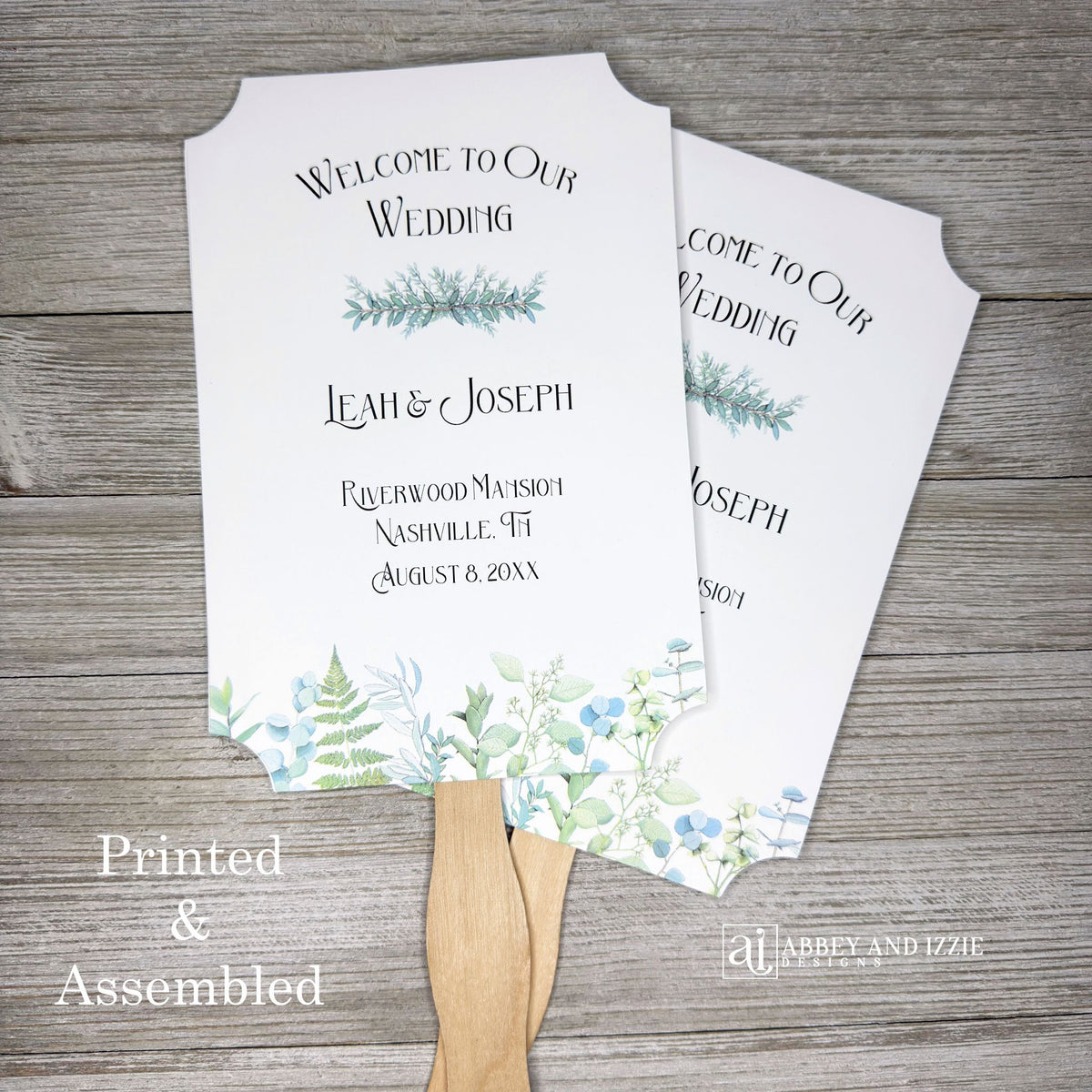 Greenery Wedding Favor Fans personalized and shipped assembled.  White fans with  bride and grooms names, date and wedding location.  Delicate greenery printed at the bottom, corners are cut out, wooden handle is hidden between layers.