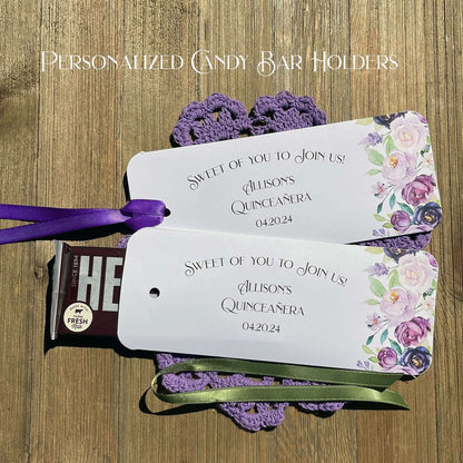 Personalized Quinceanera Candy Favors printed on white card stock and adonred with purple flowers.  Each printed with 'sweet of you to join us' with the guest of honors name and event date.  Slide a candy bar in the open end and tie the ribbon on, your choice of purple or moss green ribbon.