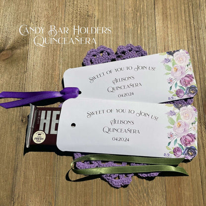 Personalized Quinceanera Candy Favors printed on white card stock and adonred with purple flowers.  Each printed with 'sweet of you to join us' with the guest of honors name and event date.  Slide a candy bar in the open end and tie the ribbon on, your choice of purple or moss green ribbon.