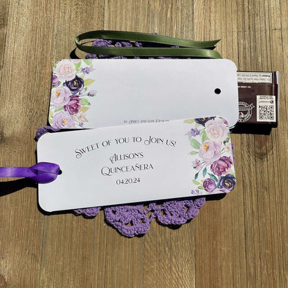 Personalized Quinceanera Candy Favors printed on white card stock and adonred with purple flowers.  Each printed with 'sweet of you to join us' with the guest of honors name and event date.  Slide a candy bar in the open end and tie the ribbon on, your choice of purple or moss green ribbon.