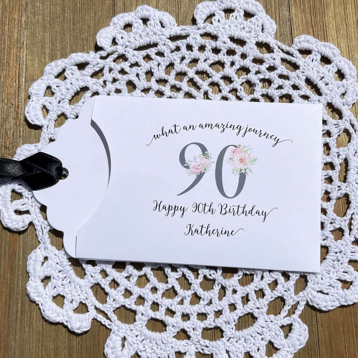 Elegant 90th Birthday Party Favors will add a special touch to your event.  Printed on white card stock with a large 90 in floral font add the guest of honors name for a personal touch.  Your choice of pink, black or white ribbon which comes attahced.