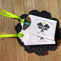 Pickleball party favors that will be fun for all your guests.  Adonred with a pickleball and paddles these are personalized for the event.  Printed on white cardstock with green ribbon attached.  Slide a lottery ticket in the open end and see who wins.
