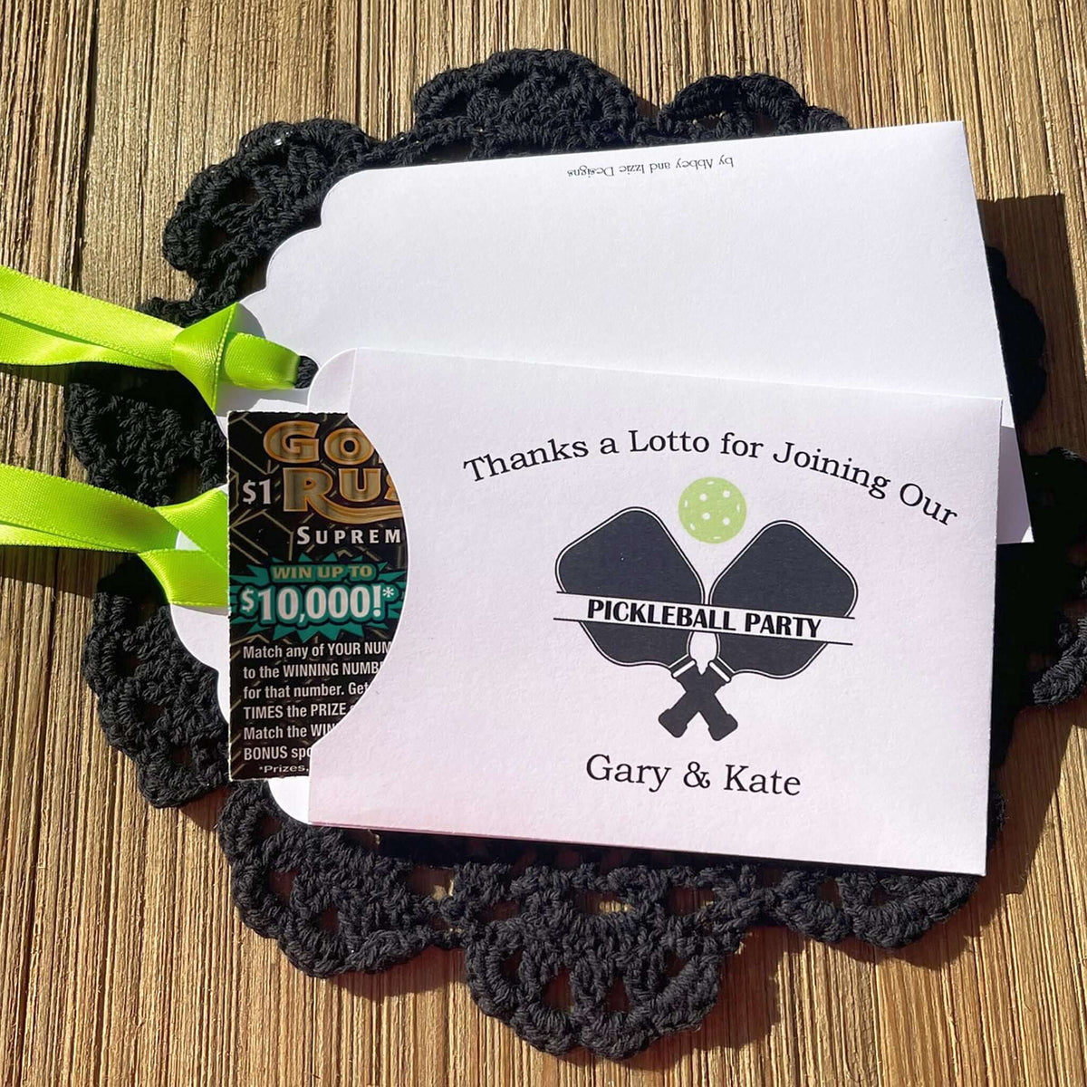 Personalized Pickleball Party Favors that will be fun for all your guests. Adonred with a pickleball and paddles these are personalized for the event. Printed on white cardstock with green ribbon attached. Slide a lottery ticket in the open end and see who wins.
