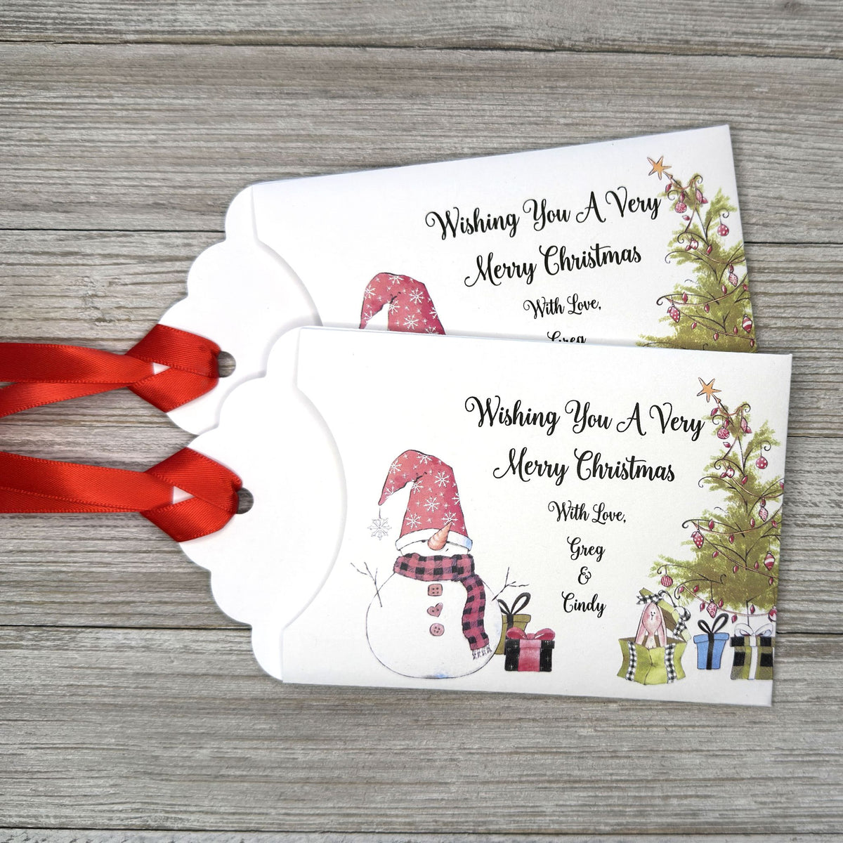 Small Christmas gift lottery ticket envelopes, give your guests a chance to win big. Enclose a scratch off lotto ticket, just a little something to remember friends or co-workers this Holiday Season.  Envelopes are made from white cardstock with a snowman, Christmas tree and gifts.  Personalized with wishing you a Very Merry Christmas. Red ribbon comes attached.