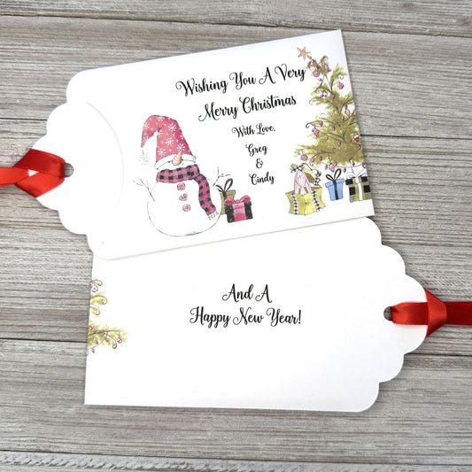 Small Christmas gift lottery ticket envelopes, give your guests a chance to win big. Enclose a scratch off lotto ticket, just a little something to remember friends or co-workers this Holiday Season.  Envelopes are made from white cardstock with a snowman, Christmas tree and gifts.  Personalized with wishing you a Very Merry Christmas. Red ribbon comes attached.