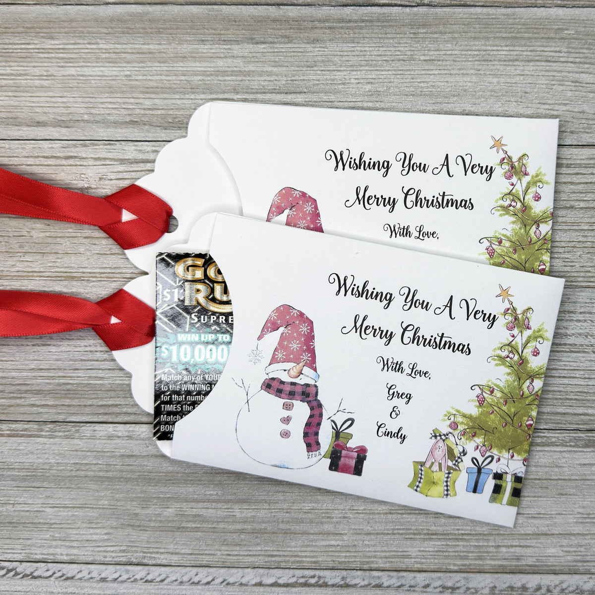 Small Christmas gift lottery ticket envelopes, give your guests a chance to win big. Enclose a scratch off lotto ticket, just a little something to remember friends or co-workers this Holiday Season.  Envelopes are made from white cardstock with a snowman, Christmas tree and gifts.  Personalized with wishing you a Very Merry Christmas. Red ribbon comes attached.