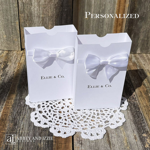 White favor boxes personalized for the guest of honor.  Made from white card stock with white ribbon around the box and a white satin bow attached.  