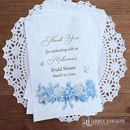 Personalized blue hydrangea bridal shower favors bags, perfect for a small gift of appreciation or a cookie bar or even a candy bar.  White bags adorned with delicate blue hydrangeas for a sweet addition to your event.