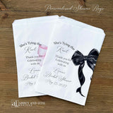 Send your guests home with a memorable keepsake from the bride-to-be's special day with our She's Tying the Knot Bridal Shower Favor Bags . These charming favor bags feature a playful "She's Tying the Knot" design that perfectly captures the excitement of bridal shower celebrations.  Adorned with a black or Pink bow, your choice and personalized for the bride to be.  Printed on white bags, larger than most.