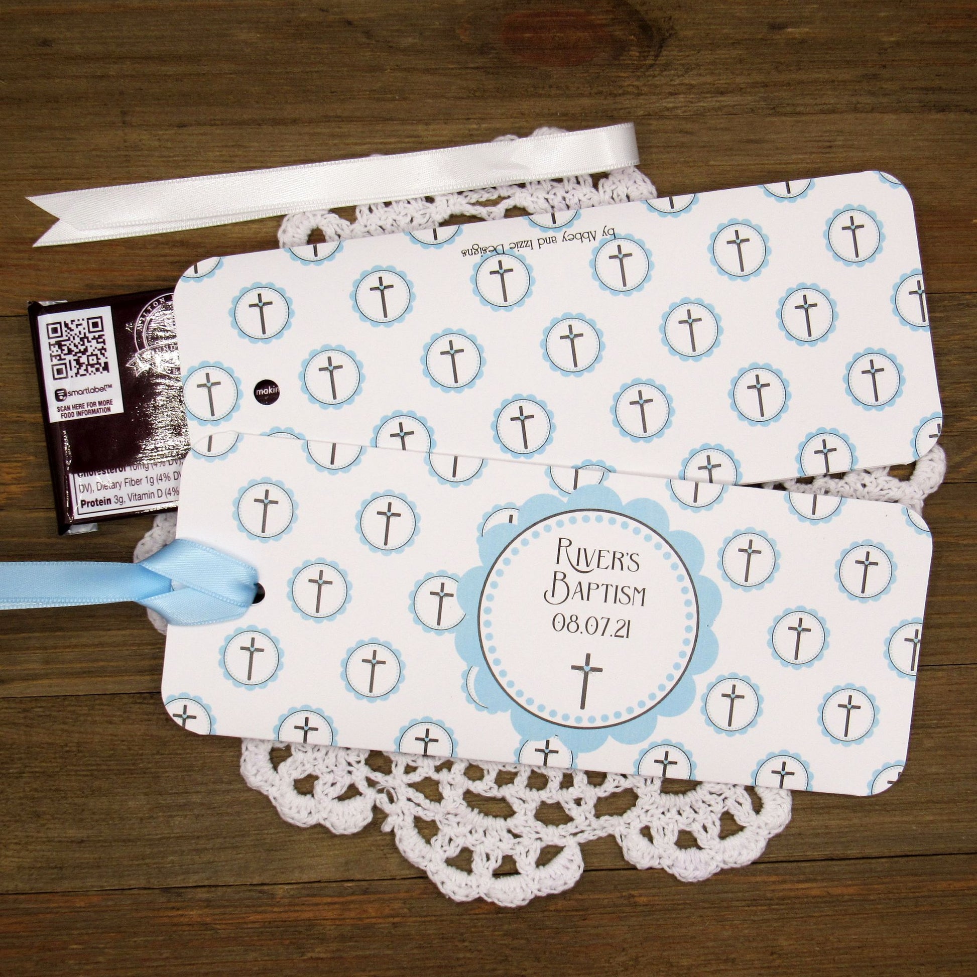 Personalized Baptism Party Favors for Baby Boys.  Printed on white card stock adorned with blue crosses with babies name and baptism date.  Choice of light blue or white ribbon which is included and left off for easy filling.  Slide a candy bar in the open end and tie the ribbon.