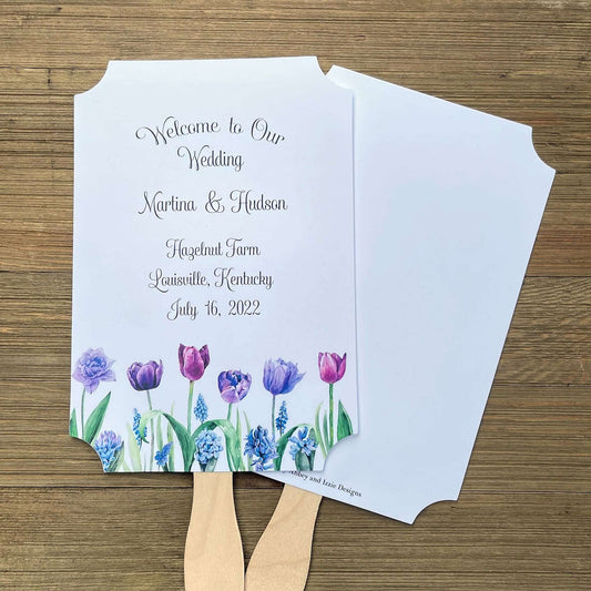 Tulip Wedding Guest Fans adorned with purple tulips.  Fans are printed on white card stock, two sided with handle hidden between, printing on one side only.  Printing included bride and groom, place, city and state and date.  Shipped assembled with wooden handle attached.