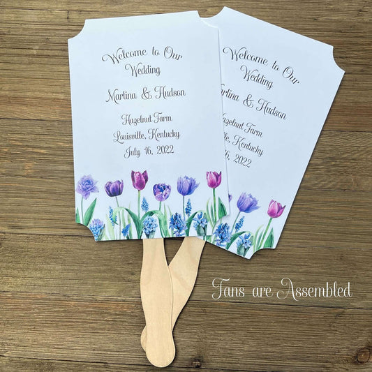 Tulip Wedding Guest Fans adorned with purple tulips.  Fans are printed on white card stock, two sided with handle hidden between, printing on one side only.  Printing included bride and groom, place, city and state and date.  Shipped assembled with wooden handle attached.
